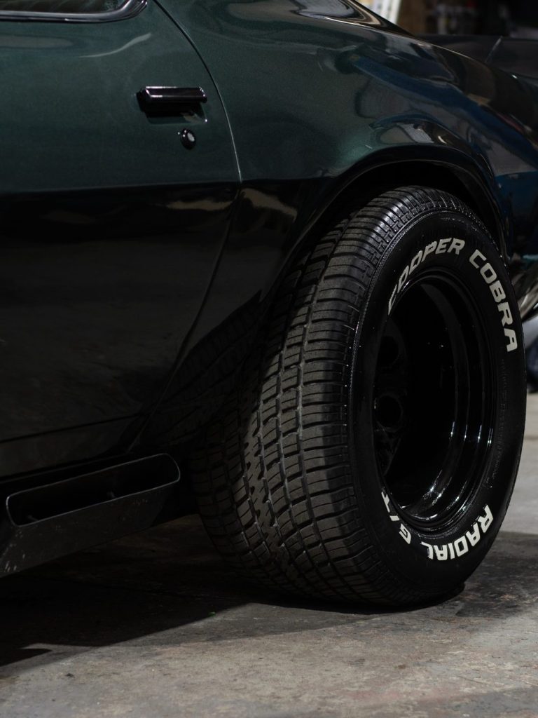 Dark green Camaro rear wheel in a workshop with Cooper text on the sidewall